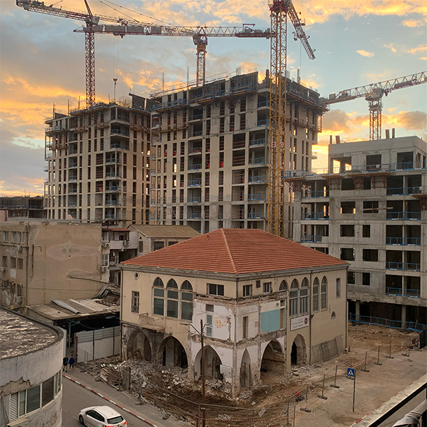 Sunset over the filthy concrete. Half-ruins of an old Arab well house surrounded by crumbling semi-industrial mid-rises, while behind it all cranes tower over the concrete skeletons of skyscrapers that are yet to be