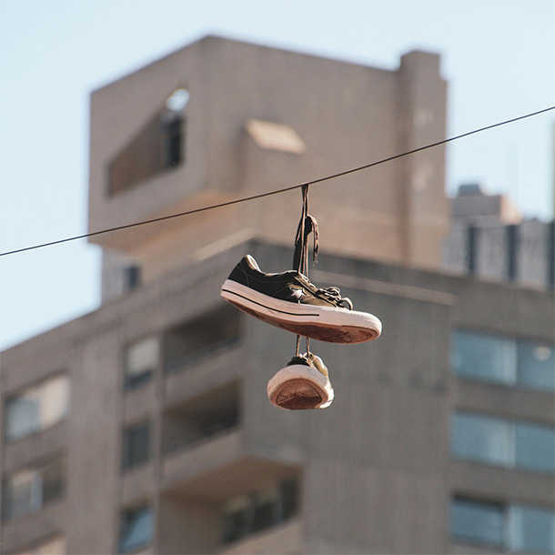 A pair of shoes hanging from a black wire; an out-of-focus apartment building looms behind