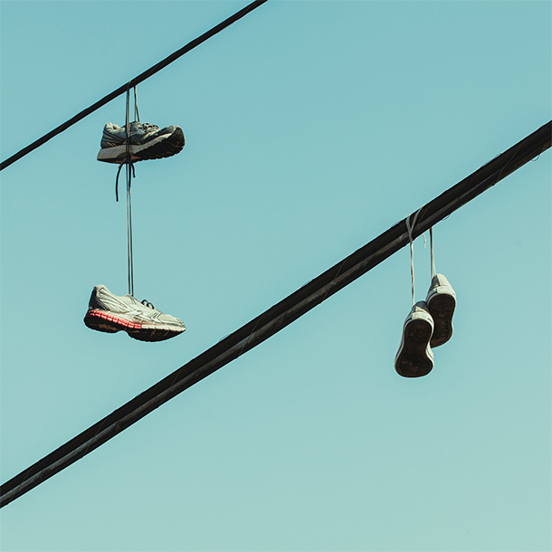 Power cables cut diagonally across a blue-green sky; pairs of shoes dangle off of them
