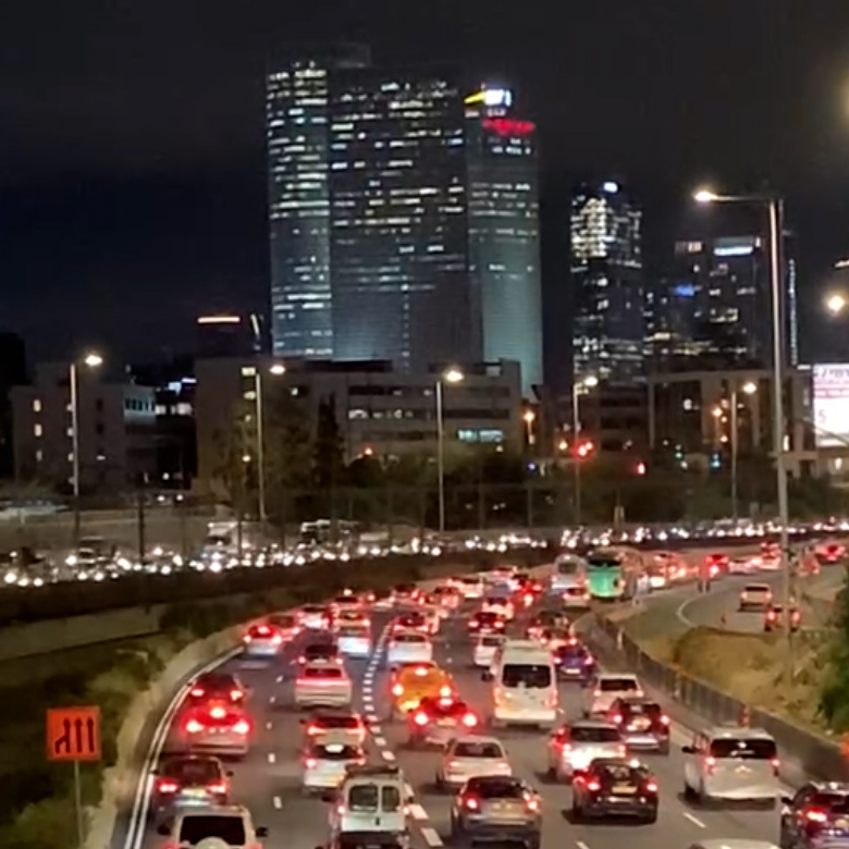 Grainy photo of an urban freeway at night; an ocean of brakelights below lit-up skyscrapers