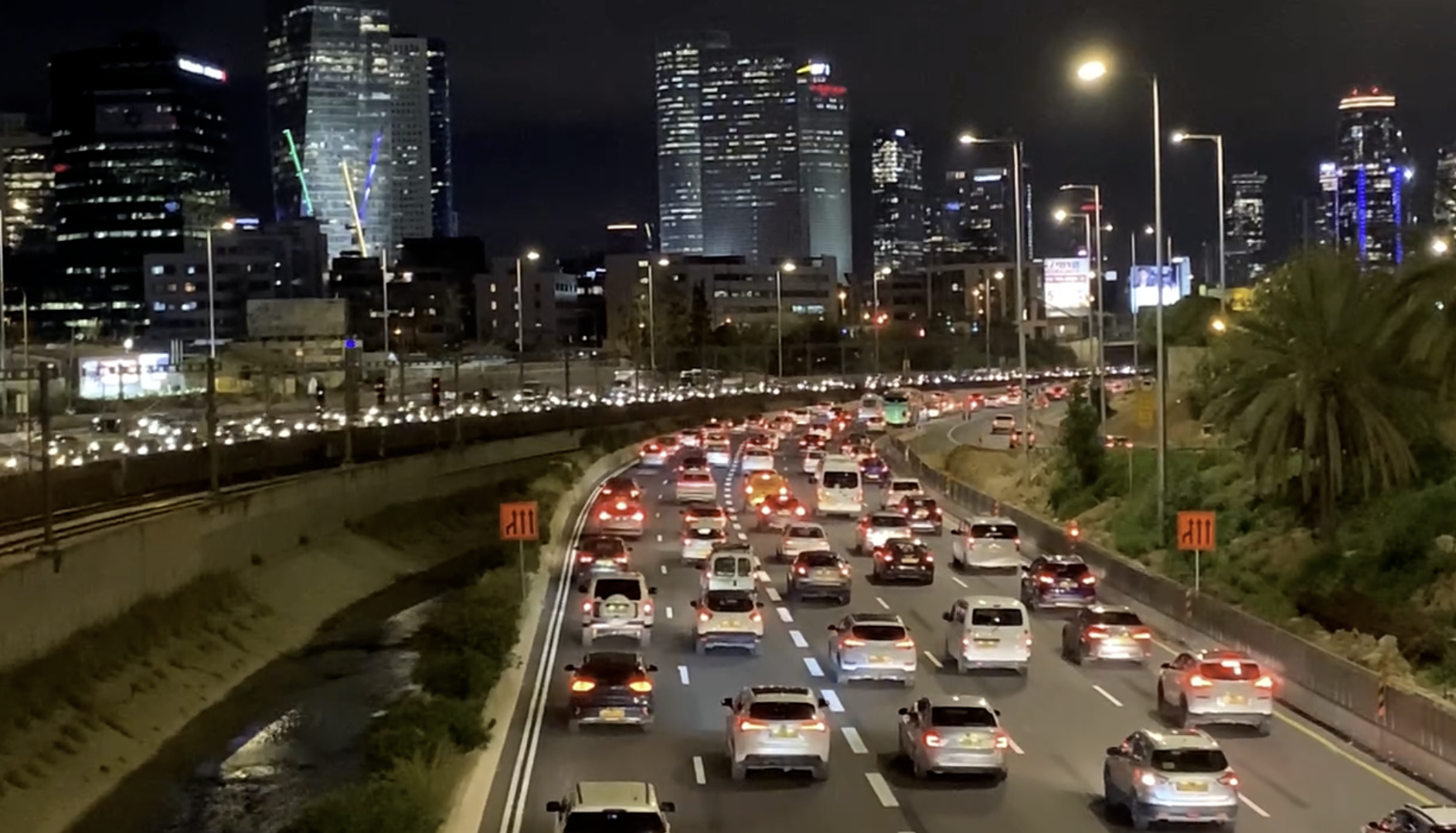 A photo of the Ayalon Freeway at night. Five lanes in each direction, clogged up with cars, with a concrete canal and three railroad tracks running down the middle. Office buildings and skyscrapers in the background twinkle their lights, like the stars that this city hadn't seen for decades, above the ocean of brakelights to the right, and a stream of headlights to the left.