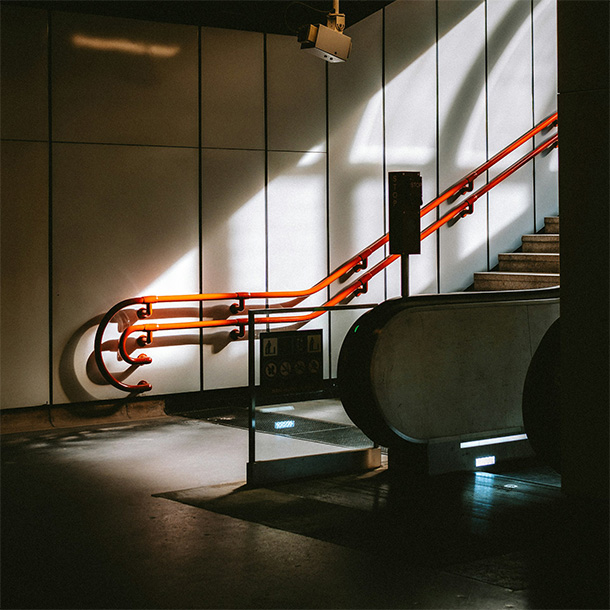 Stairs and escalator leading out of a dark subway staiton in Vienna; rays of light cast rectangles and arches on the wall